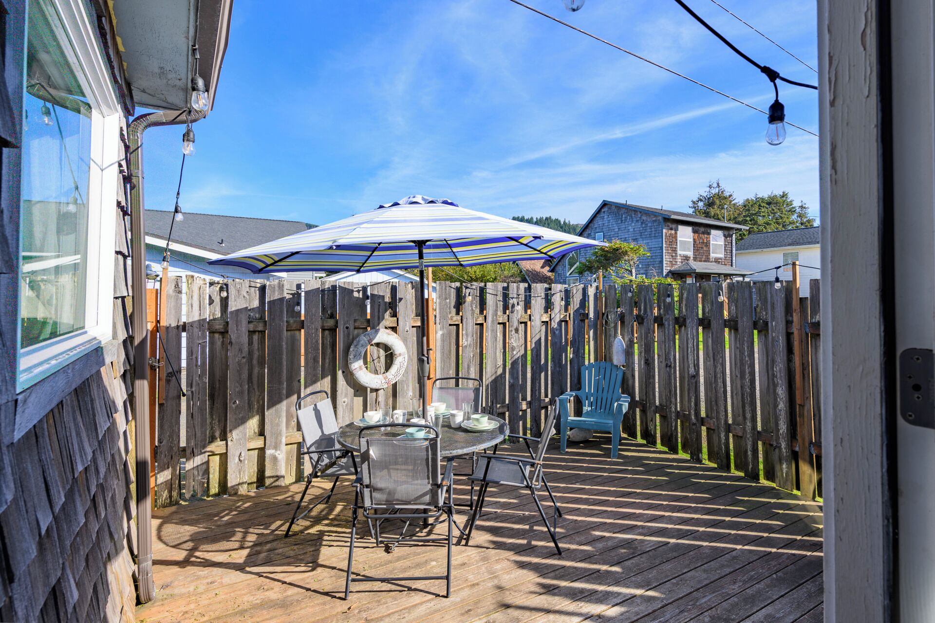 Une terrasse en bois avec une table et des chaises, une chaise bleue et un parasol à rayures.