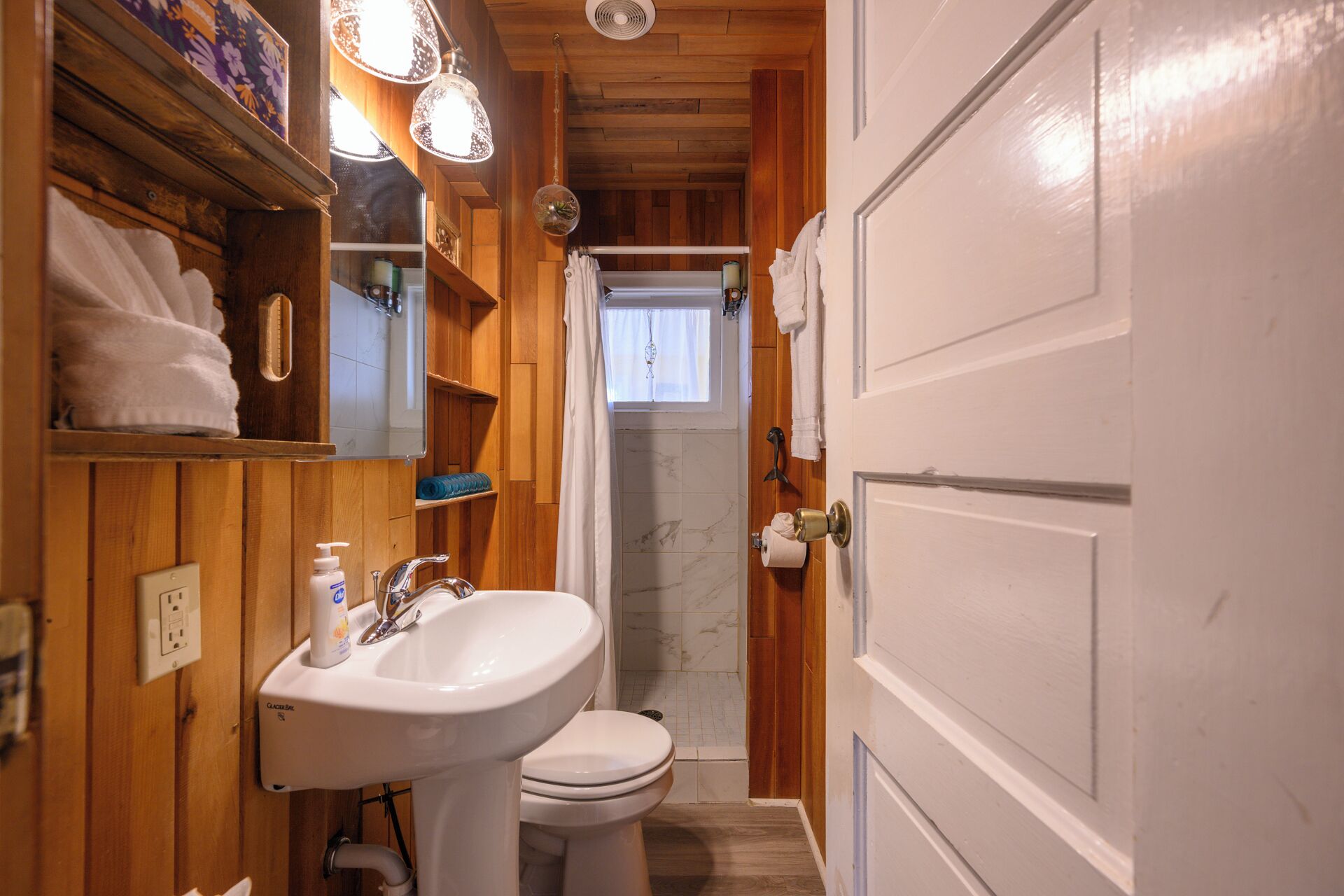 Een kleine badkamer met houten inrichting, een witte wastafel, toilet en douchehoek.