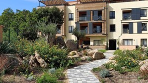 Un immeuble moderne à plusieurs étages, doté de balcons, d’un chemin pavé et de jardins aménagés.