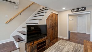 A staircase with a TV on a wooden console, a sign reading "AIRPLANE HANGAR," and a door in the background.