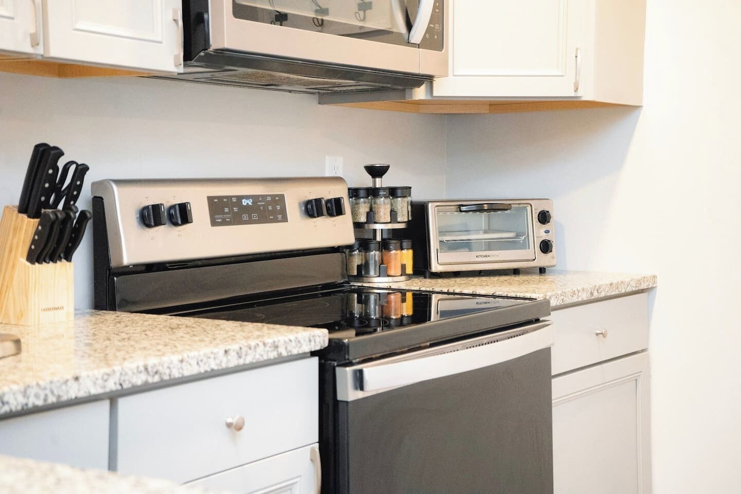 A kitchen with a stove, microwave, and toaster. There is a spice rack and a knife block on the counter.