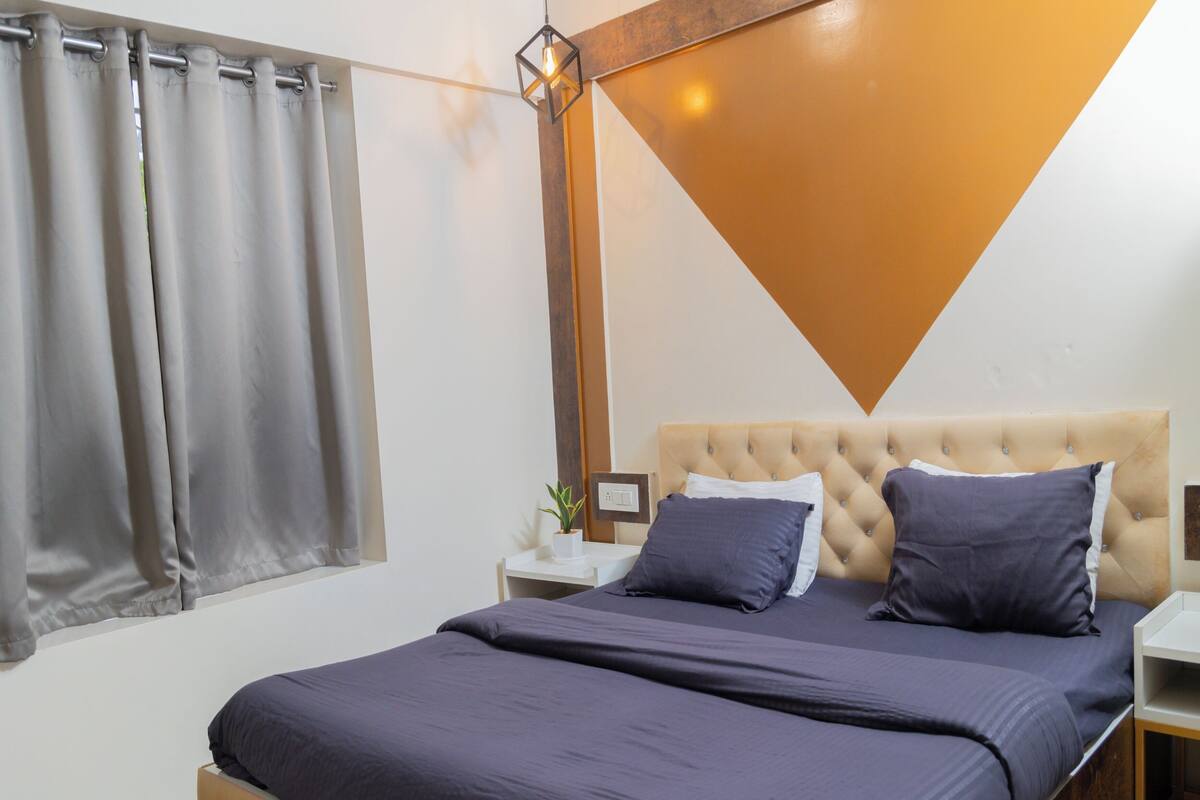 A bedroom with a bed, nightstands, a potted plant, and a geometric wall design.