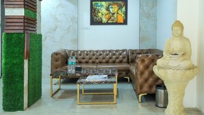 A living room with a brown leather sofa, a glass coffee table, a Buddha statue, and a painting on the wall. - Copper 11 Service Apartments -SB Road, Shivaji Nagar, Pune (Pune)