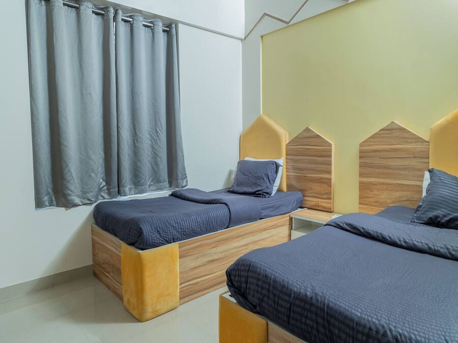 Un dormitorio moderno con dos camas de madera, ropa de cama gris y una ventana con cortinas grises.