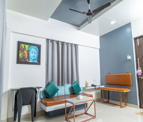 A modern living room with a sofa, a coffee table, a ceiling fan, and a painting on the wall. - Copper 11 Service Apartments -SB Road, Shivaji Nagar, Pune (Pune)