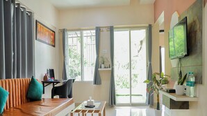 A modern living room with a sofa, a coffee table, a TV mounted on the wall, and a sliding glass door leading to an outdoor area. - Copper 11 Service Apartments -SB Road, Shivaji Nagar, Pune (Pune)