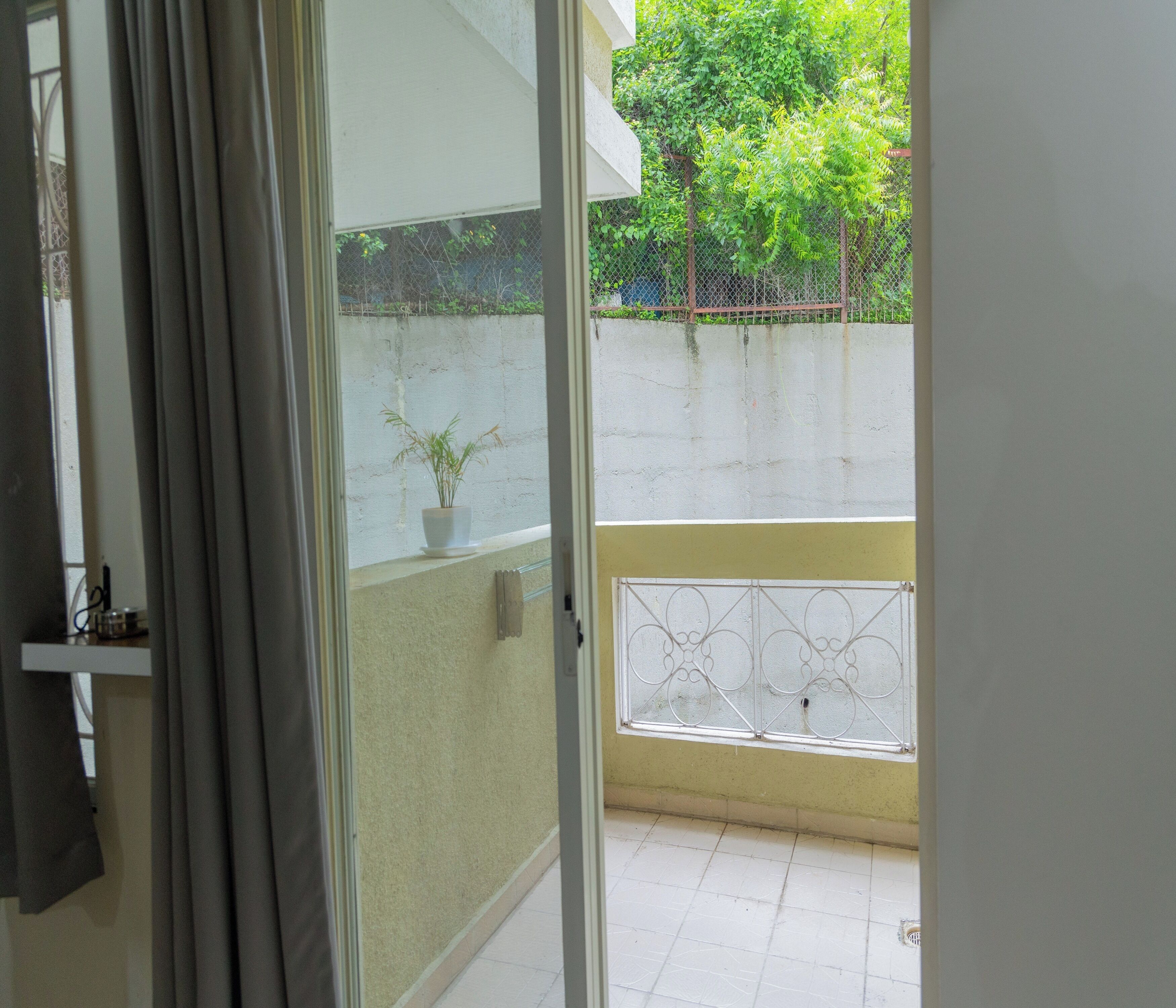 Blick durch eine offene Tür auf einen Balkon mit einem Blumentopf, einem Metallgeländer und einer Betonwand.