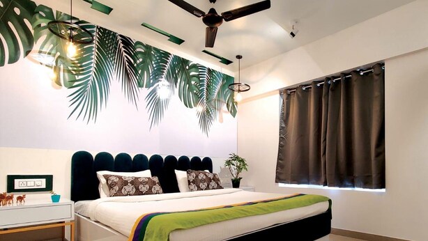 A modern bedroom with a bed, a ceiling fan, a window with curtains, and a wall with a leaf pattern. - Copper 11 Service Apartments -SB Road, Shivaji Nagar, Pune (Pune)