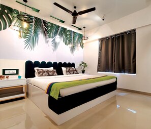 A modern bedroom with a bed, a ceiling fan, a window with curtains, and a wall with a leaf pattern. - Copper 11 Service Apartments -SB Road, Shivaji Nagar, Pune (Pune)