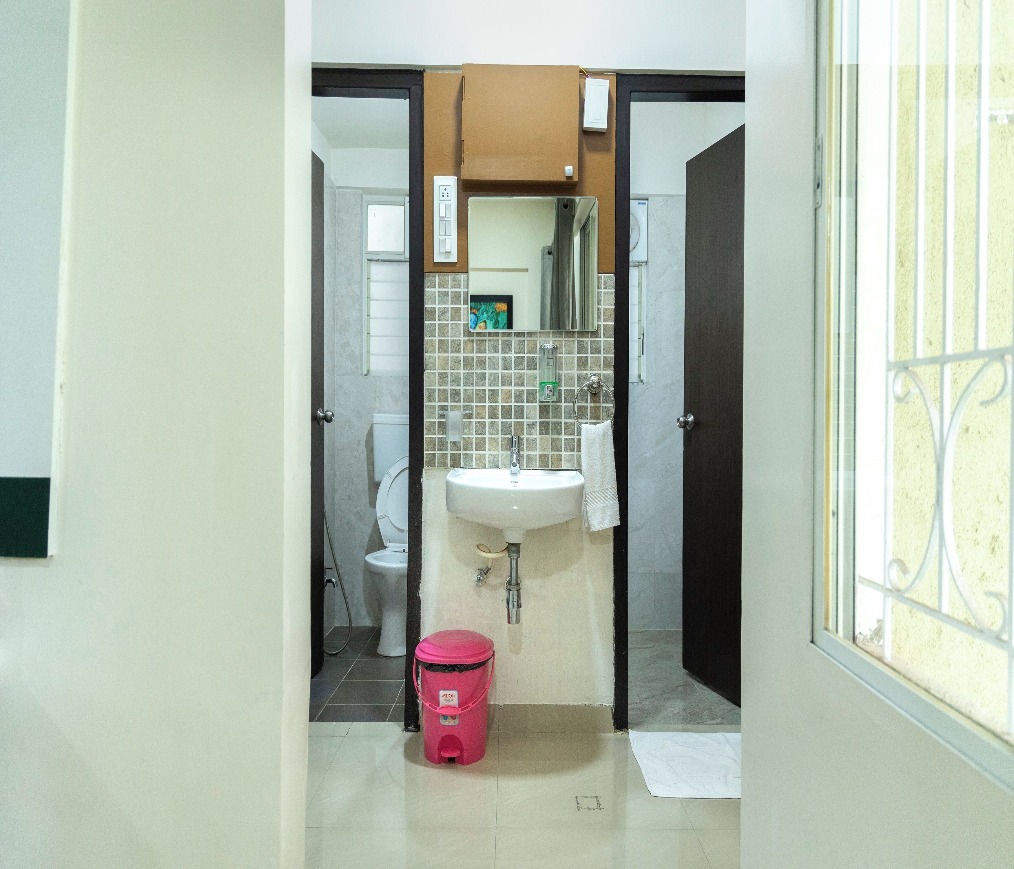 A bathroom with a toilet, sink, and a pink trash bin.
