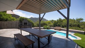 Une terrasse extérieure couverte avec une piscine, un barbecue et une table et un banc en bois.