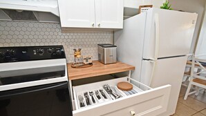 Eine kleine Küche mit weißen Schränken, einem schwarzen Herd, einer eingebauten Kaffeemaschine und einem Kühlschrank.