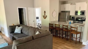 A living room with a grey sofa and a kitchen area with white cabinets and a stainless steel refrigerator. - Creekside Cottage-kayaks/fire pit/pet friendly (Jacksons' Gap)
