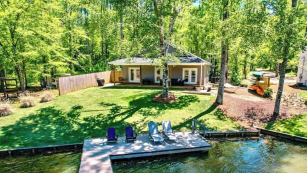 A house with a dock extending into a pond, surrounded by a well-maintained lawn and trees. - Creekside Cottage-kayaks/fire pit/pet friendly (Jacksons' Gap)