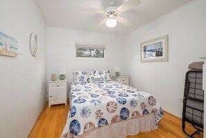 Une chambre à coucher avec un lit, un ventilateur de plafond, une fenêtre et une table de chevet avec une lampe.