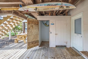 Une terrasse en bois avec une table de pique-nique, une porte portant l’inscription « PRIVÉ » et une planche de surf accrochée au-dessus.