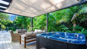 Une terrasse extérieure dotée d’un jacuzzi, de meubles en osier et d’une végétation luxuriante.