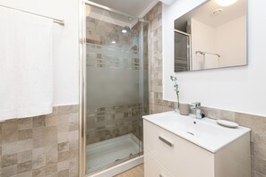 Ein modernes Badezimmer mit einer gläsernen Dusche, einem weißen Waschbecken und einem Spiegel darüber.
