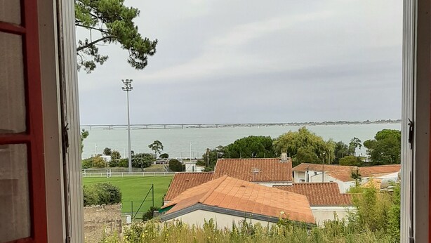 A view from a window with a view of a patio area, a table with chairs, and a distant bridge.