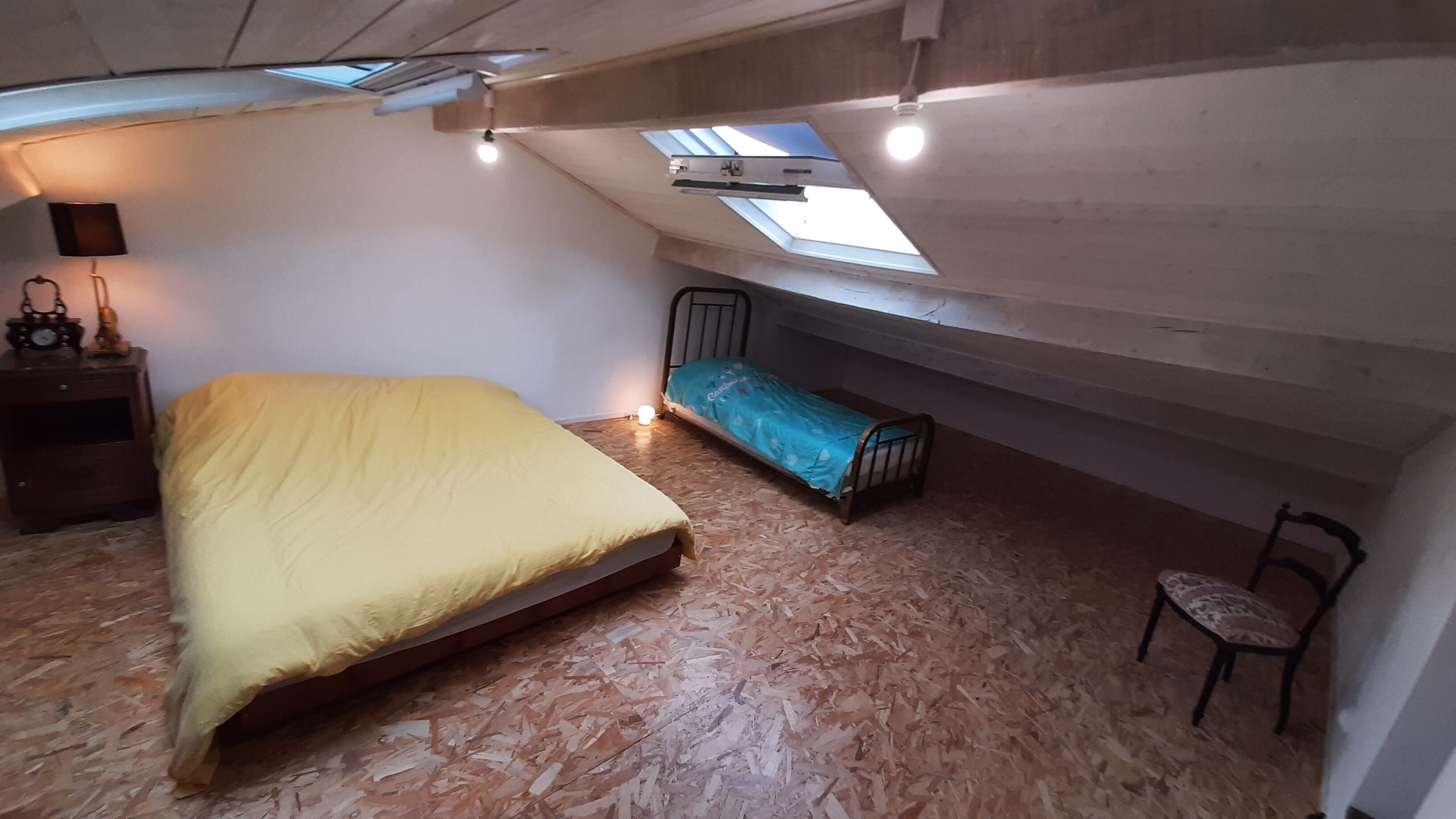 Ein kleiner, kompakter Raum mit Etagenbett, einem Einzelbett, einem Sessel und einem Schreibtisch mit Lampe. Über dem Etagenbett befindet sich ein Dachfenster.