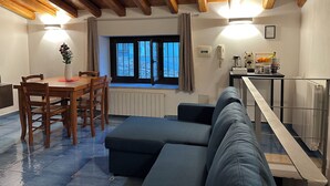 Una habitación acogedora con techo de madera, un comedor con mesa y sillas, un sofá y una ventana con cortinas.