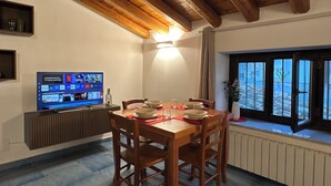 Un área de comedor con una mesa y sillas de madera, un televisor mostrando un servicio de streaming, y una ventana con vistas al exterior.
