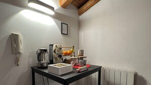 Una kitchenette pequeña con cafetera, hervidor de agua, frutero y una caja de selección de tés.