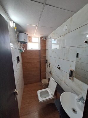 A compact bathroom with a toilet, sink, and a small window. - Meadows Inn (Mysore)
