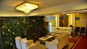A lobby with a reception desk, seating area, and a decorative wall. - Meadows Inn (Mysore)