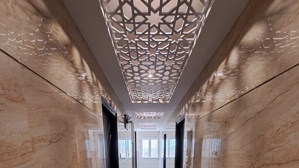 A hallway with patterned floor tiles, a decorative ceiling, and modern doors. - Meadows Inn (Mysore)