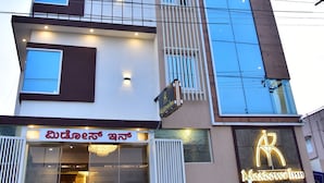 A multi-story hotel with a modern design, featuring a prominent 'Best A/C Rooms' sign and a neon 'Metropolis Inn' sign. - Meadows Inn (Mysore)