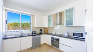 Een moderne keuken met witte kasten, een vaatwasser, een oven, een magnetron en een raam met uitzicht op groen.