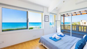 Een slaapkamer met een groot raam dat uitkijkt over de zee, een balkon met uitzicht, en een opgemaakt bed.