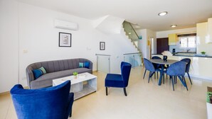 Una sala de estar moderna con un sofá gris, sillas azules, una mesa de centro y una escalera que lleva a una cocina.