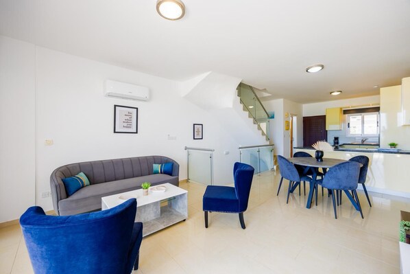 Una sala de estar moderna con un sofá gris, sillas azules, una mesa de centro y una escalera que lleva a una cocina.