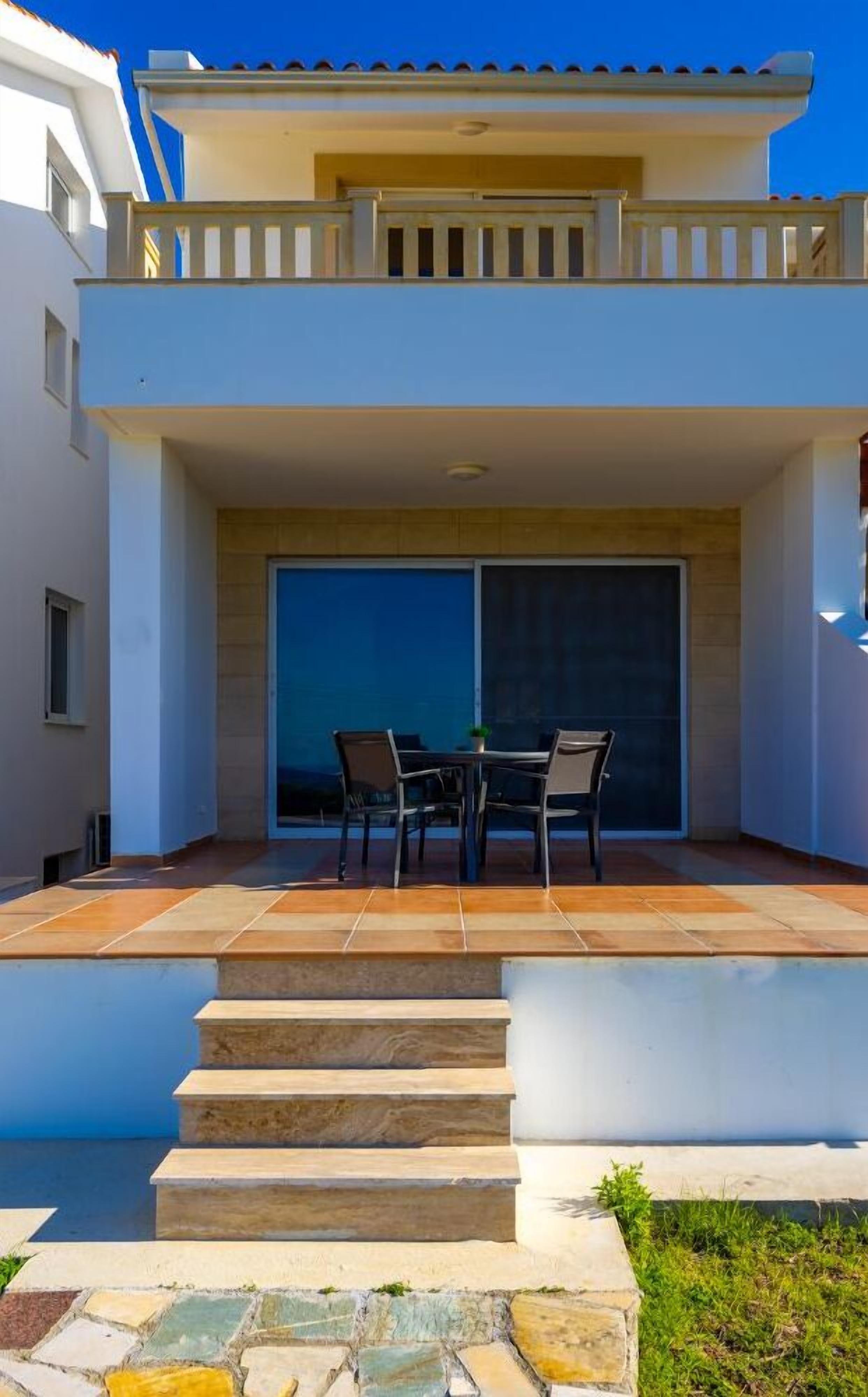 A modern two-story building with a patio area featuring a table and chairs, a large sliding glass door, and a staircase leading to the upper level.