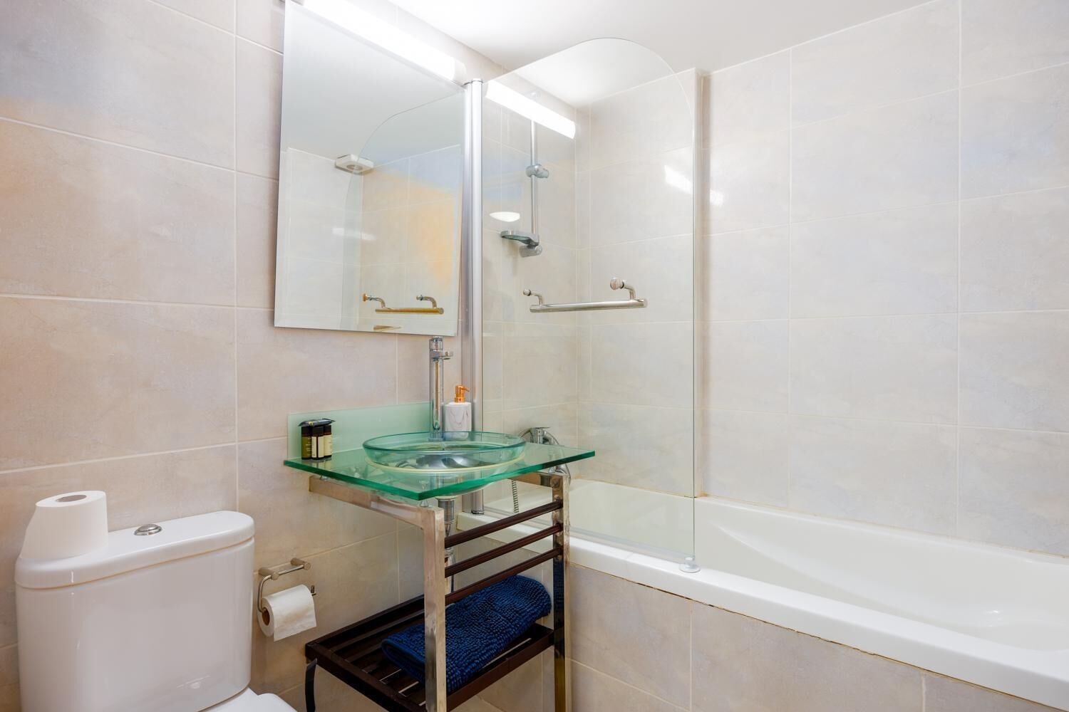 Un baño moderno con lavamanos de vidrio, inodoro, ducha y bañera.