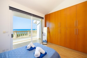 Una camera da letto con un letto, un armadio, uno specchio e un balcone vista mare.