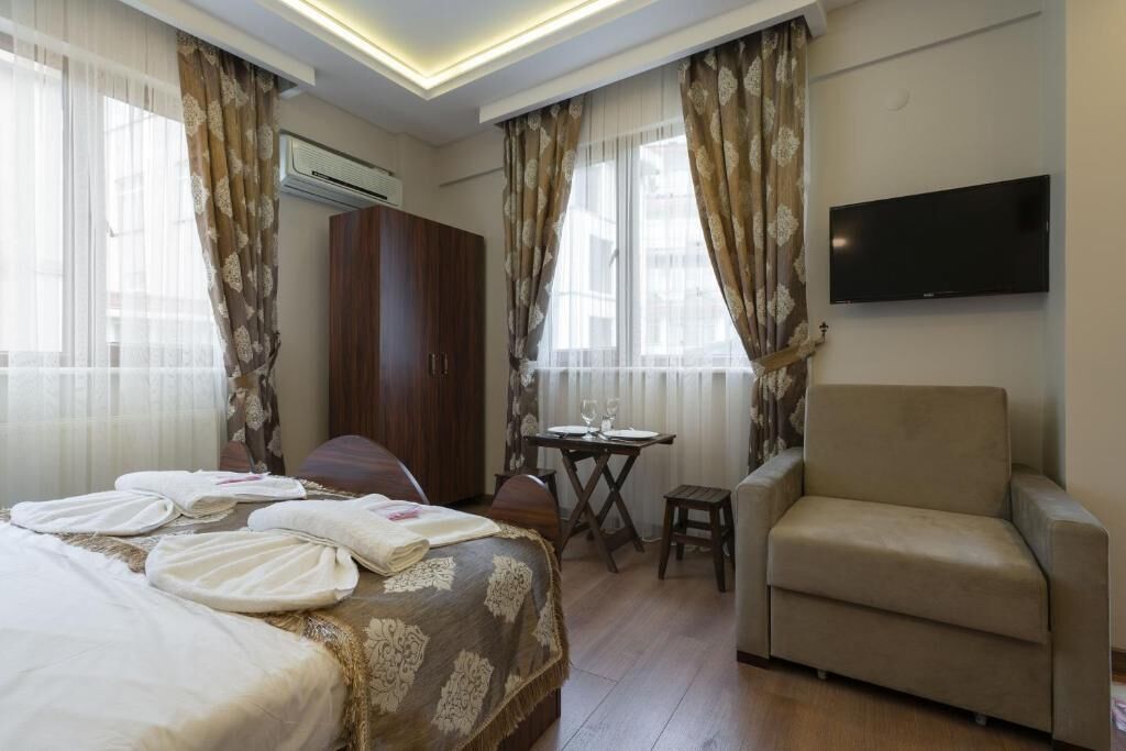 Hotellihuone, jossa on sänky, sohva, televisio ja pieni pöytä sekä tuoli.