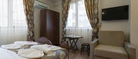 A hotel room with a bed, a sofa, a TV, and a small table with a chair.