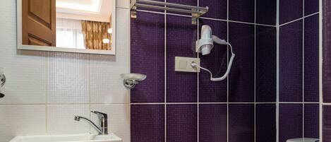 A bathroom with a white sink, mirror, and toilet, and purple tiled walls.