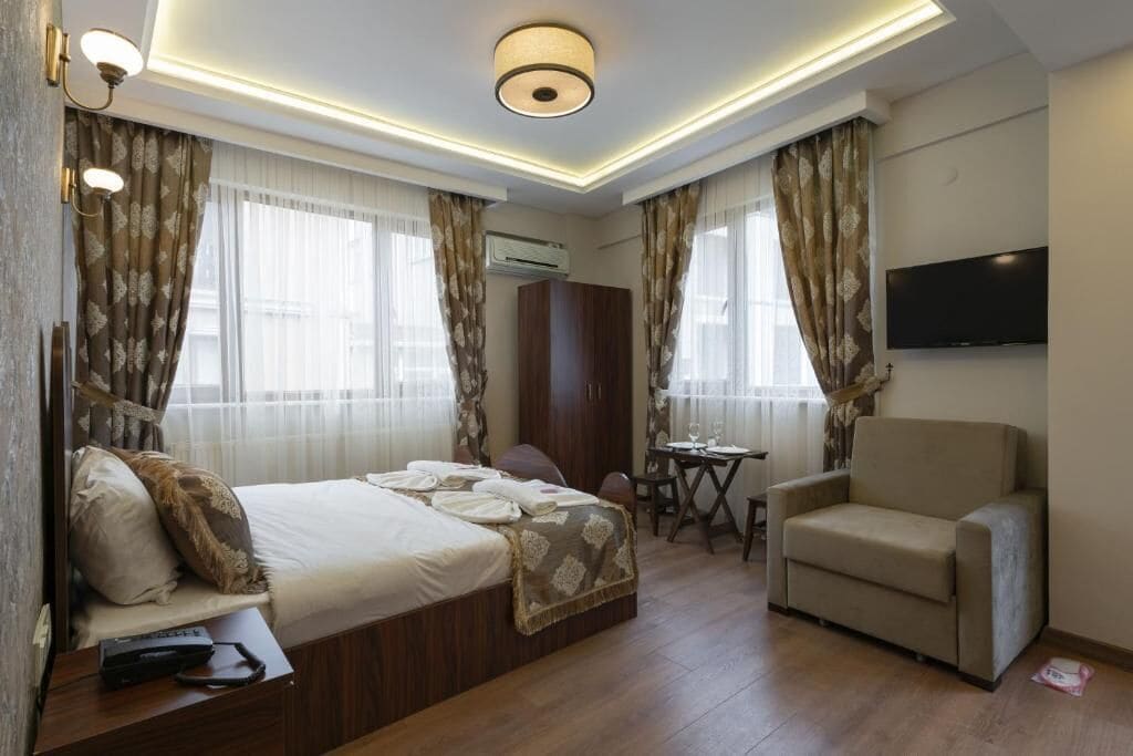 A hotel room with a bed, a chair, a TV, and a table.
