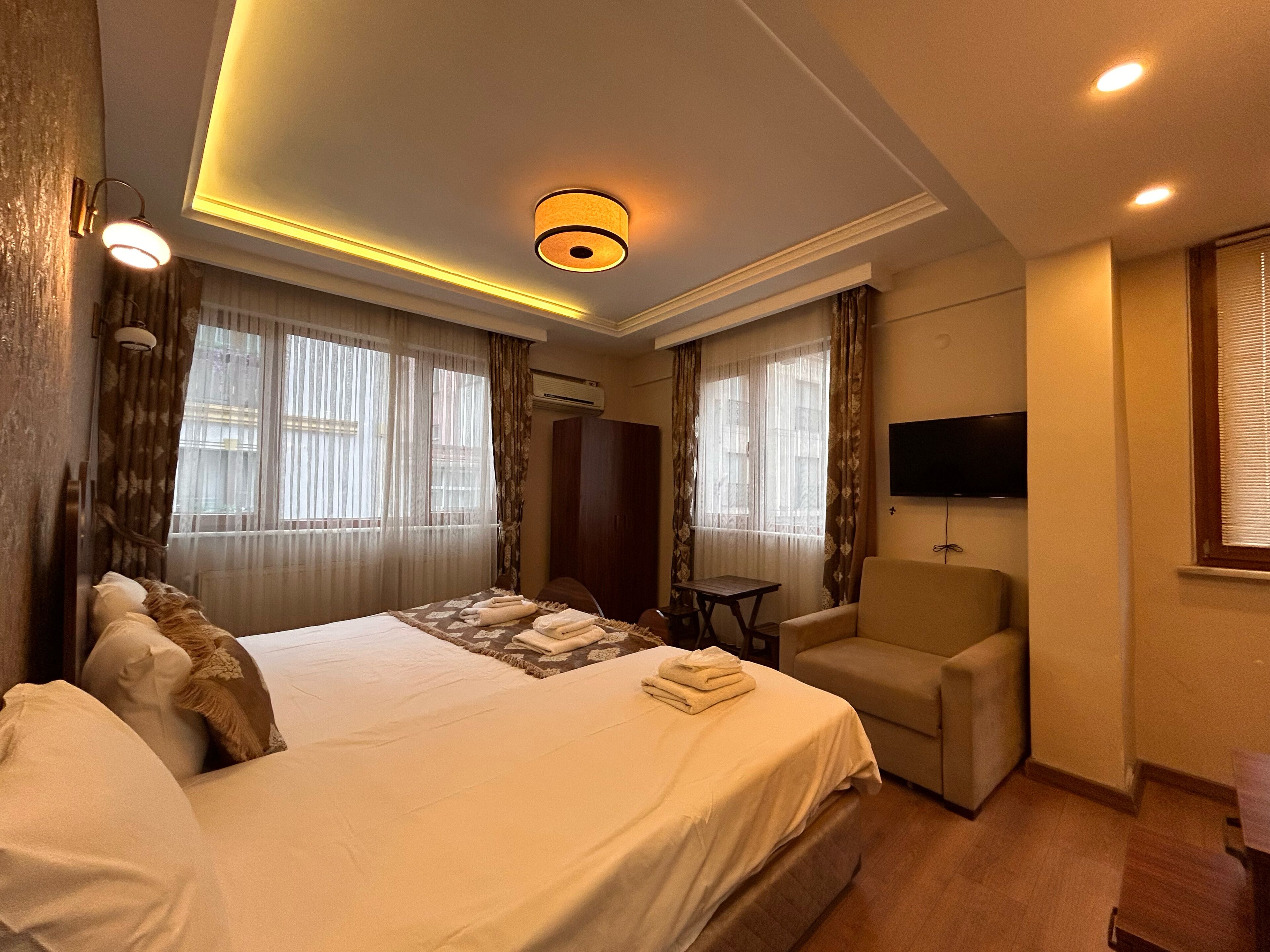 A hotel room with a large bed, a seating area, a television, and a window with curtains.