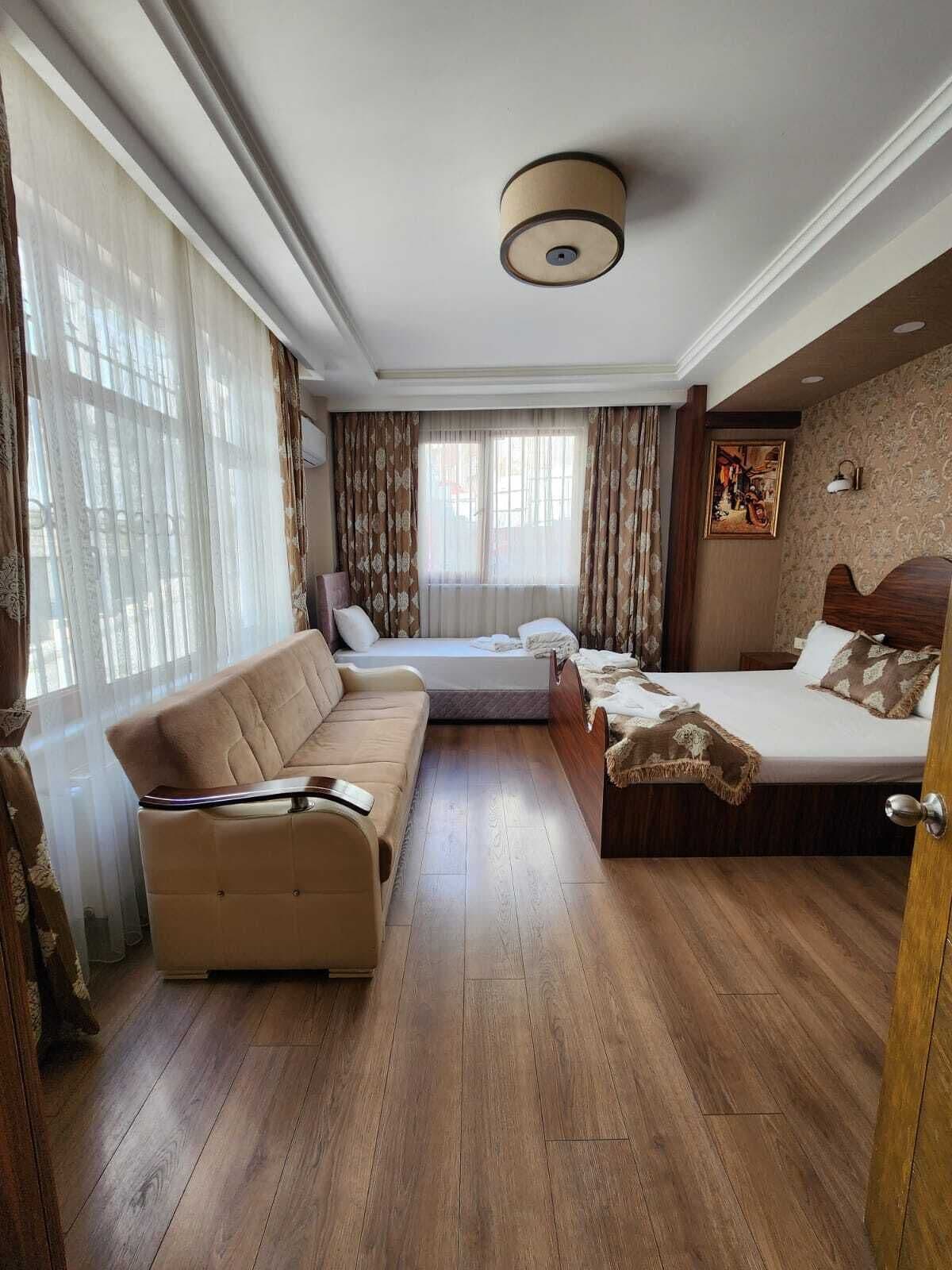Une chambre d’hôtel avec un canapé, deux lits, un plancher en bois, un luminaire au plafond et un tableau au mur.