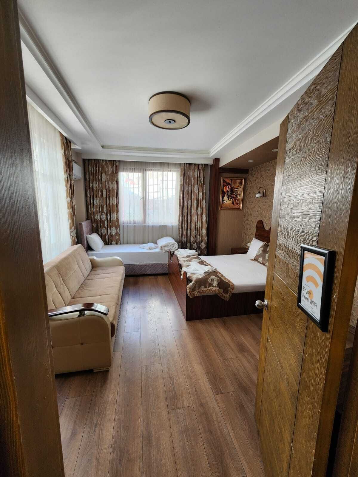 A hotel room with a sofa, two beds, a ceiling light, and a door with a sign offering free WiFi.