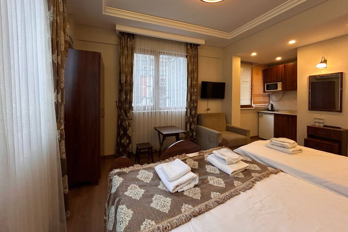 A hotel room with a bed, a desk, a chair, a television, and a kitchenette.