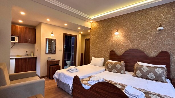 A hotel room with a double bed, a small bedside table, a chair, a bathroom with a toilet and sink, and a kitchenette with a microwave. - Capricorn by Otantik Suites (Istanbul)