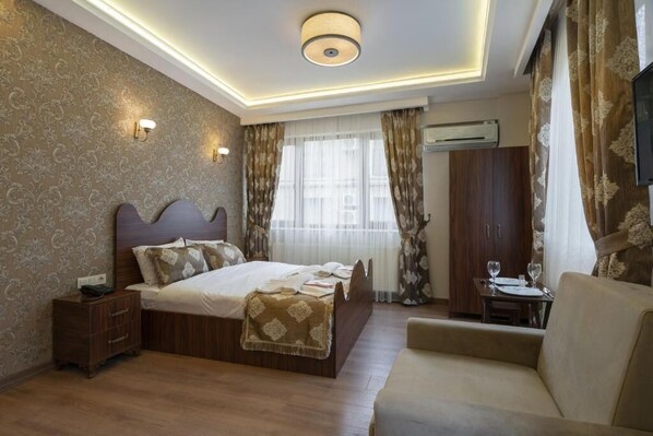 Une chambre d’hôtel avec un grand lit, une table de chevet, un canapé, une petite table avec des verres et un téléviseur fixé au mur.