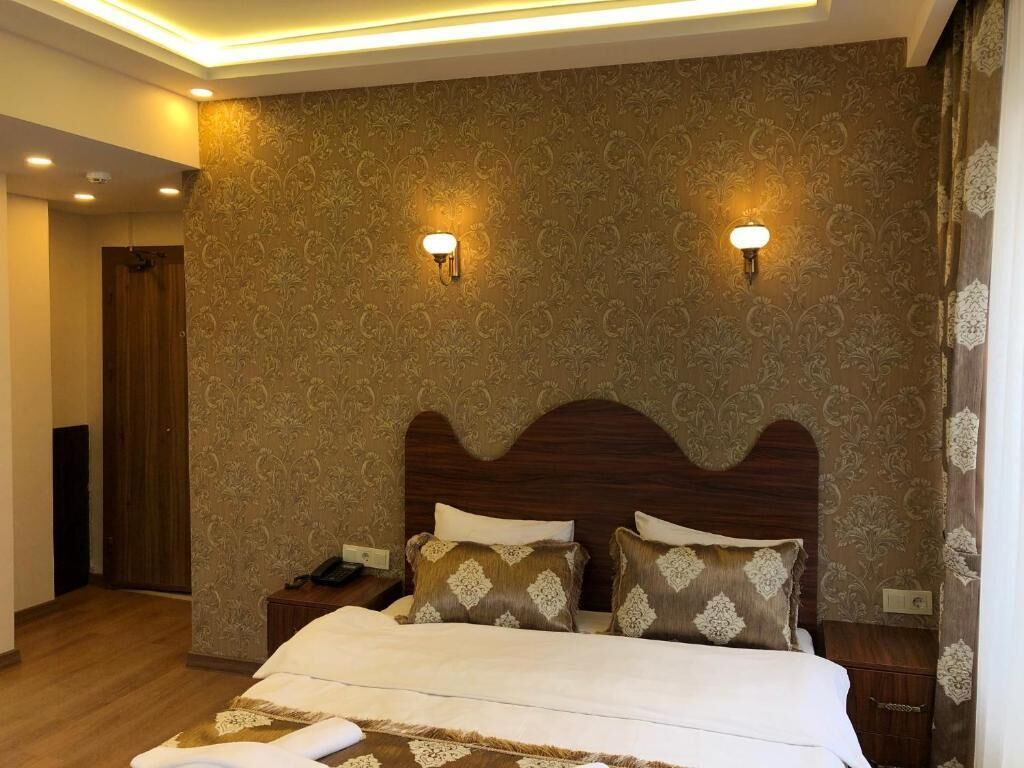 Une chambre d’hôtel avec un grand lit, deux tables de chevet, une tête de lit en bois et un papier peint à motifs.