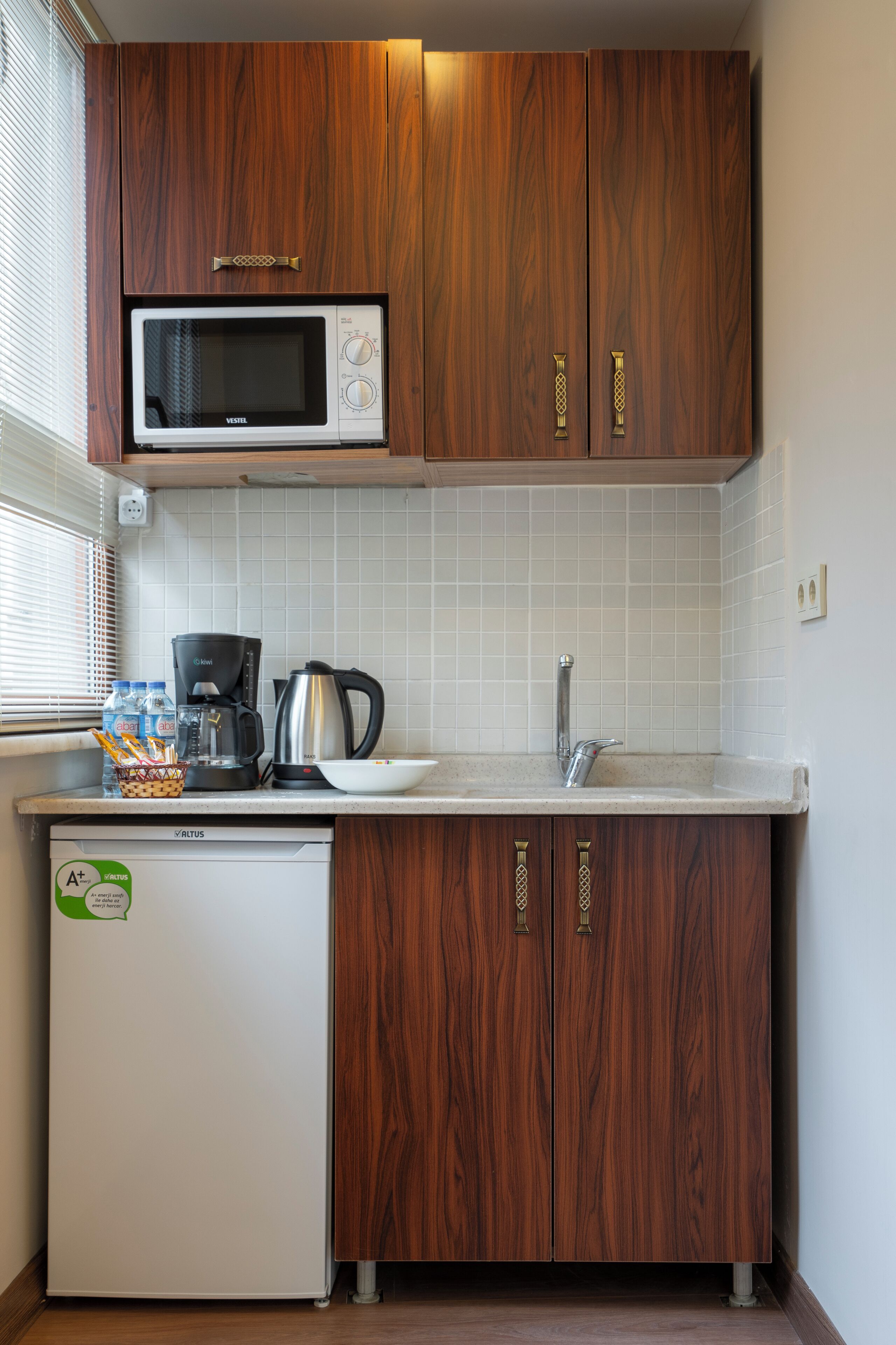 A compact kitchen with wooden cabinets, a microwave, a coffee maker, and a refrigerator.